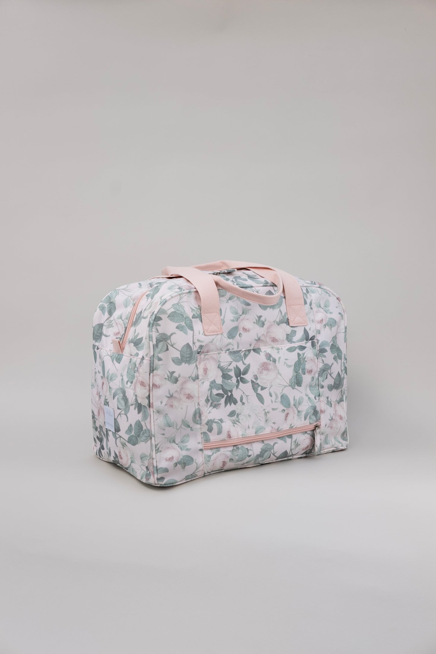 Floral patterned bag with pink straps on a gray background. Shows back of duffle with exterior pocket.