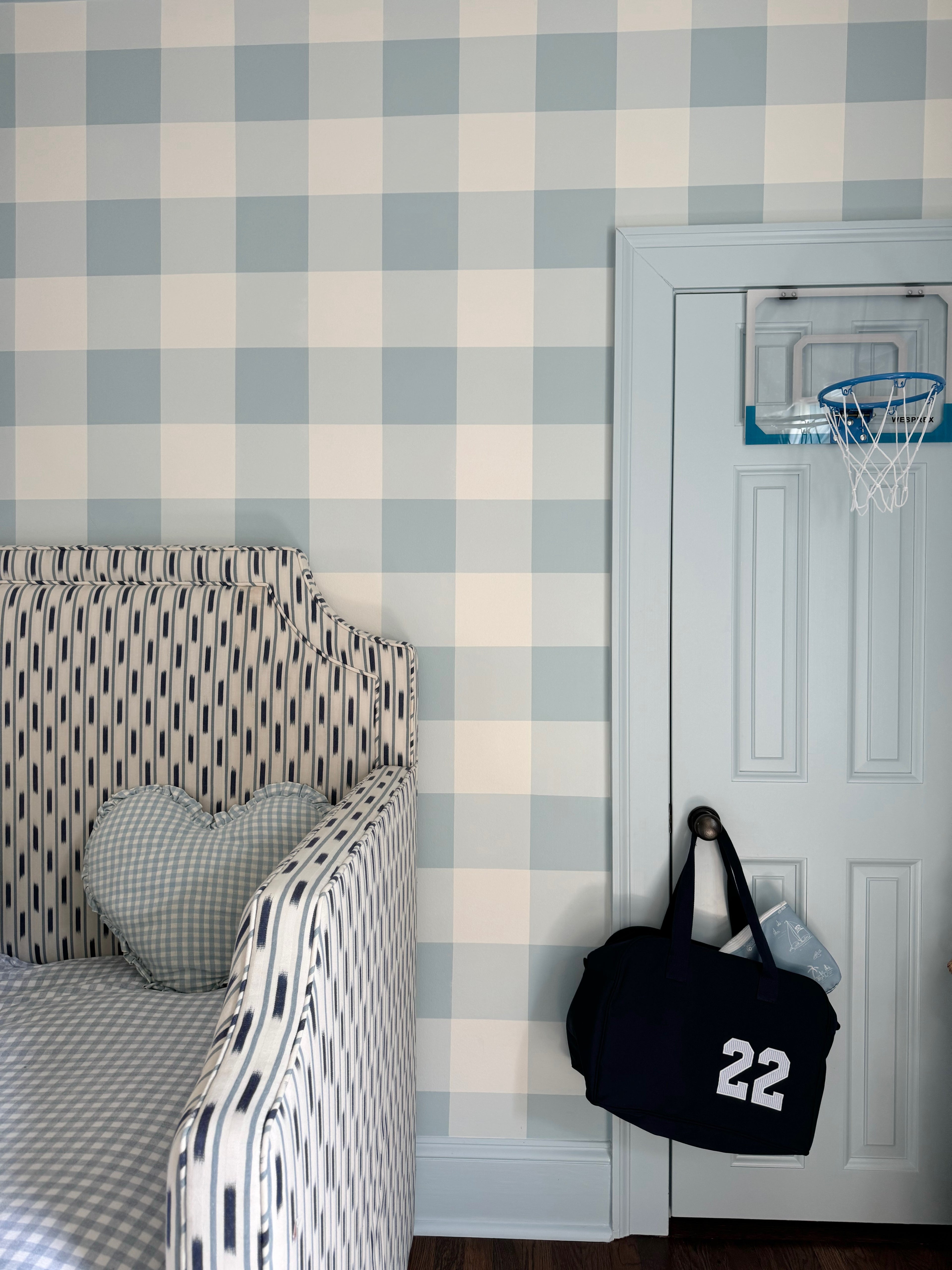 Bedroom with checkered wallpaper, bed, and door with sports bag and basketball hoop.