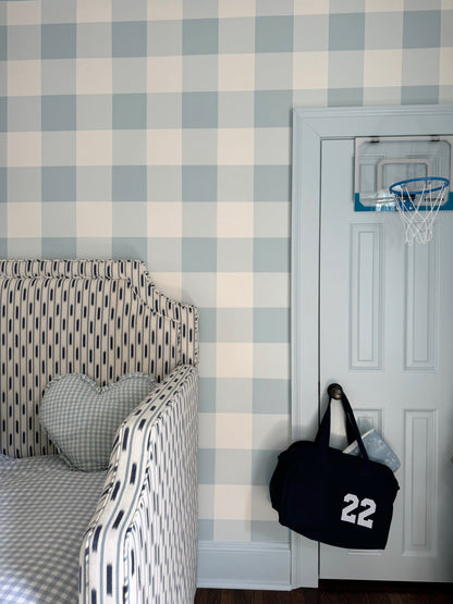 Bedroom with checkered wallpaper, bed, and door with sports bag and basketball hoop.