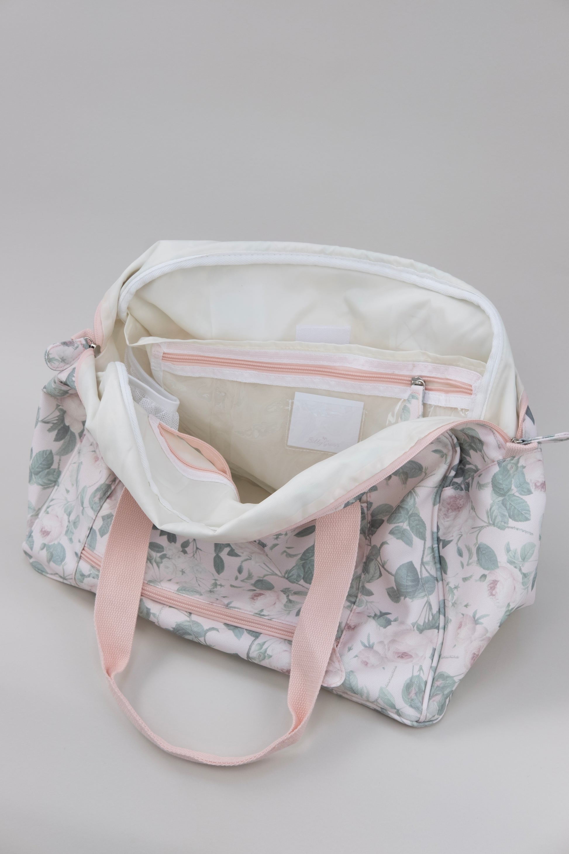 Inside view of label pockets on the floral-patterned duffle bag with pink straps on a light gray background