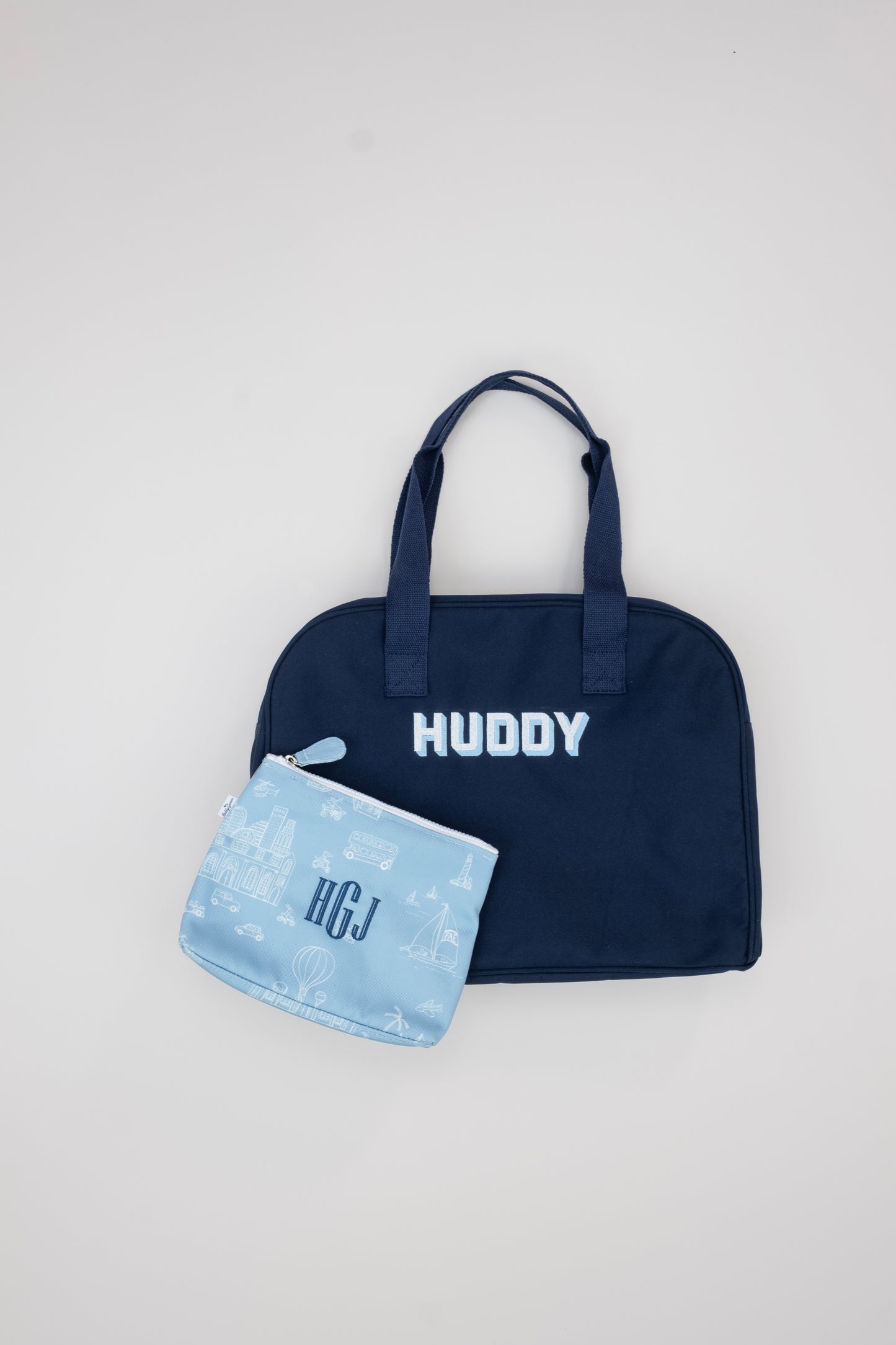Navy tote bag with 'HUDDY' personalization and a blue patterned pouch on a light gray background